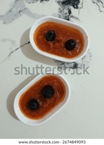 Two small plates with garlic-rubbed tomatoes and two olives isolated on a white background