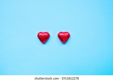 Two Small Red Hearts On Light Blue Background, Chocolate Candy Wrapped In Tinfoil.