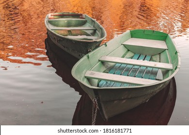 Two small rowboats are anchored at coast of a still lake