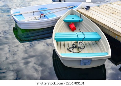 Two small wide white fiberglass dixie dingy boats moored at a wooden floating wharf. The skiff is used to transport as a tender between vessels at a pier. The shells have oars and buoys in the boats. 