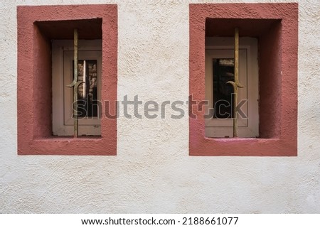 Two small windows framed in red in a white wall with roughcast