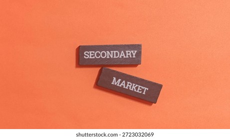 Two small wooden rectangular blocks inscribed with the words secondary and market are positioned against a solid bright orange textured surface.