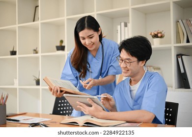 Two smart young Asian medical students are discussing their medical cases and researching medical papers in a library together. - Powered by Shutterstock