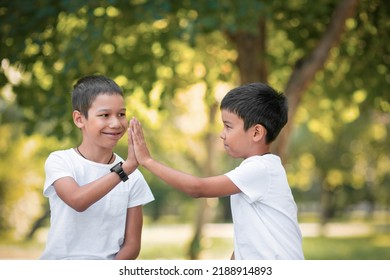 Two smiling asian boys does a high-five gesture. Brothers have fun outdoor in the public park in summer, close-up, selective focus. Children issues, leisure time, togetherness, friendship concept - Powered by Shutterstock