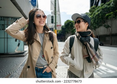 two smiling asian chinese female coworkers chatting happily on pedestrian walk while walking to work together in san Francisco California usa.