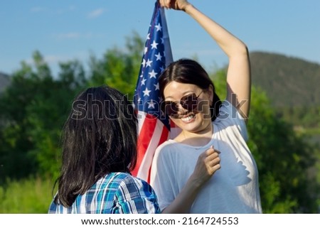 Two smiling asian woman outdoors waving USA flag, celebration of patriotic american national holiday 4th of july independence day