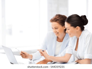 two smiling businesswomen working with laptop in office