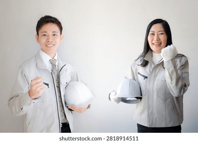 Two smiling construction workers in hard hats giving a thumbs up gesture together