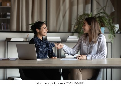 Two Smiling Diverse Young Women Corporate Workers Shake Hands Satisfied With Successful Cooperation Making Good Deal. Millennial Indian Female Employee Handshake Colleague Appreciate For Help In Work