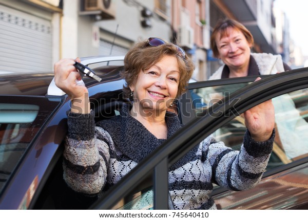 Two smiling\
elderly woman with keys near\
car