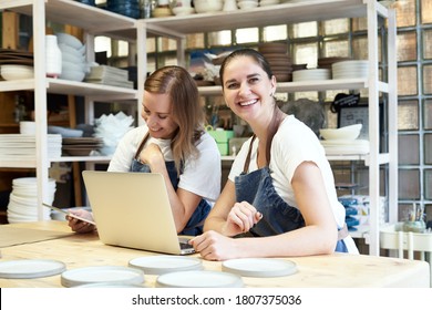 Two smiling female entrepreneur with laptop in artisan workroom. Waist up portrait of cheerful smiling woman artisan posing in pottery studio and looking at camera - Powered by Shutterstock