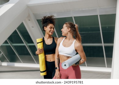 Two smiling female friend walking on morning city background with yoga mats after doing morning gym - Powered by Shutterstock
