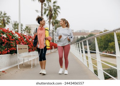 Two smiling female friend walking on morning city background with yoga mats after doing morning gym - Powered by Shutterstock