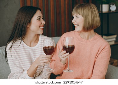 Two smiling happy fun adult women mature mom young kid wearing casual clothes drink wine put sit on gray sofa couch stay at home flat rest relax spend free spare time in living room. Family concept - Powered by Shutterstock