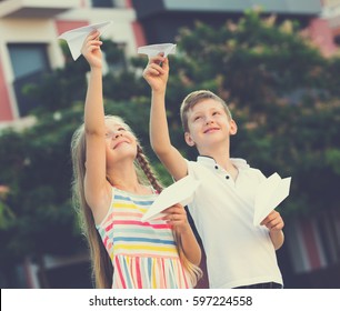 Two Smiling Kids Playing With Flying Paper Planes Outdoors