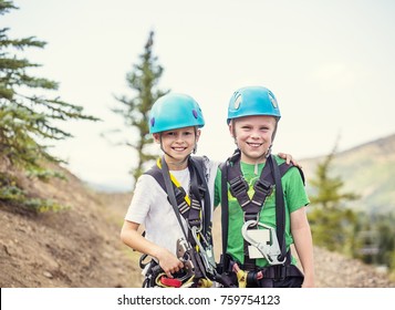 Two Smiling Kids Ready To Go On A Zip Line Adventure In The Mountains While On A Summer Vacation Together. Wearing Helmets And Having A Great Time