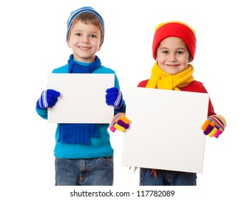 Two Smiling Kids In Winter Clothes Standing With Empty Blank In Hands, Isolated On White