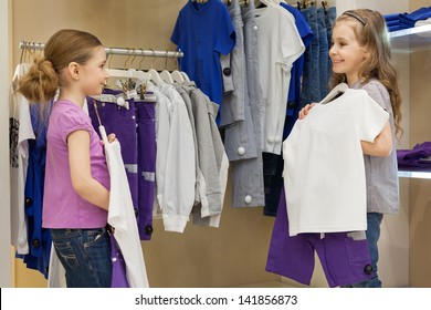 Two Smiling Little Girls Trying On The Same Dress In The Store Childrens Clothes, Focus On Right Girl