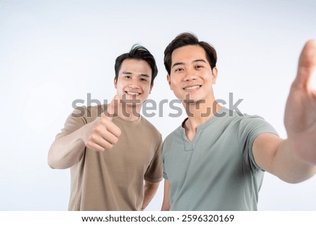 Two smiling men pose for a selfie against a white backdrop. One gives a thumbs-up, creating a cheerful and friendly atmosphere.