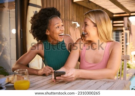 Two Smiling Multi-Cultural Female Friends Outdoors At Home Looking At Mobile Phone