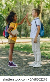 Two Smiling Multicultural Schoolkids Giving Hive Five While Standing In Park