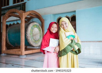 two smiling Muslim girls holding al quran book in their hands