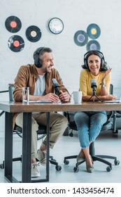 Two Smiling Radio Hosts Sitting At Workplace In Broadcasting Studio And Recording Podcast Together 