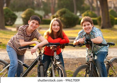 Two Smiling Teenage Boys And One Teenage Girl Having Fun On Bicycles In The Park.