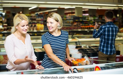 Two Smiling Women Buying Frozen Vegetables In Grocery Store. Focus On Mature Woman