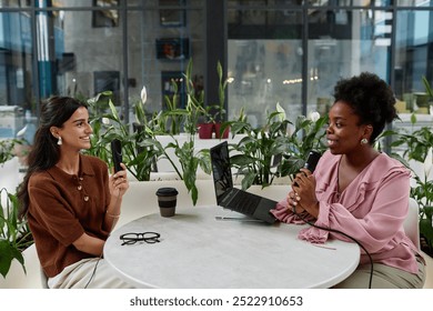 Two smiling women engaged in lively discussion about feminism co hosting podcast episode. Two successful businesswomen recording interview in cafe, copy space - Powered by Shutterstock