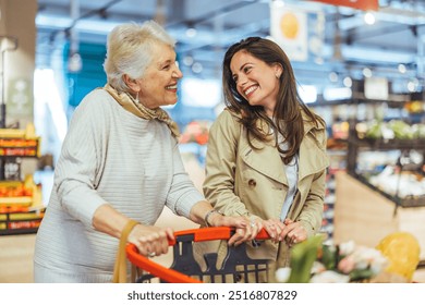 Two smiling women, a senior and a younger adult, enjoying shopping together in a grocery store, pushing a cart filled with fresh produce. - Powered by Shutterstock