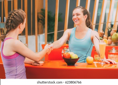 Two Smiling Women Shaking Hands At Bar In Gym