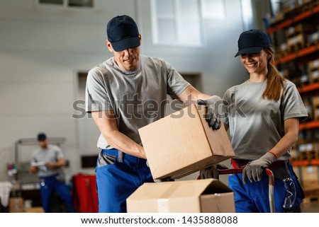 Two smiling workers loading packages and cooperating in distribution warehouse. 
