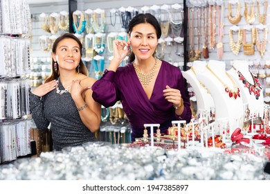 Two Smiling Young Adult Women Shopping And Trying On Imitation Jewellery In Store