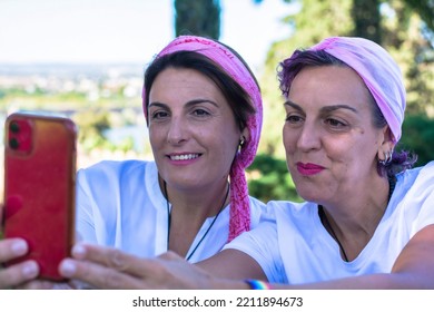 Two Smiling Young Adult Women With A Pink Headscarf Taking A Selfie. 2 Warrior Sisters Laughing And Happy After Overcoming Breast Cancer. Breast Cancer Awareness Day Concept. Warrior Women