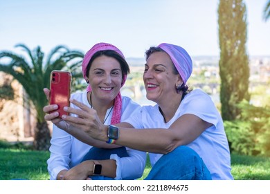 Two Smiling Young Adult Women With A Pink Headscarf Taking A Selfie. 2 Warrior Sisters Laughing And Happy After Overcoming Breast Cancer. Breast Cancer Awareness Day Concept.