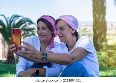 Two Smiling Young Adult Women With A Pink Headscarf Taking A Selfie. 2 Warrior Sisters Laughing And Happy After Overcoming Breast Cancer. Breast Cancer Awareness Day Concept. Family