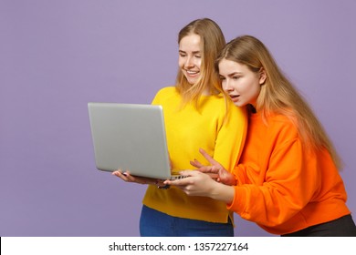 Two Smiling Young Blonde Twins Sisters Girls In Vivid Colorful Clothes Holding, Using Laptop Pc Computer Isolated On Pastel Violet Blue Background. People Family Lifestyle Concept. Mock Up Copy Space