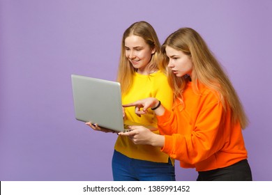 Two Smiling Young Blonde Twins Sisters Girls In Vivid Colorful Clothes Holding, Using Laptop Pc Computer Isolated On Pastel Violet Blue Background. People Family Lifestyle Concept. Mock Up Copy Space