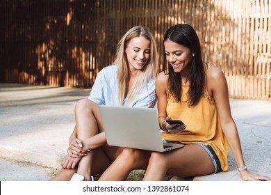 Two smiling young girls using laptop at the park, laughing, chatting - Powered by Shutterstock