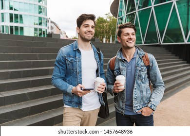 Two Smiling Young Men Friends Dressed Casually Spending Time Together At The City, Drinking Takeaway Coffee