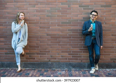 Two Smiling Young People Holding Ice Cream Cones Standing Apart Near Brick Wall With Copy Space