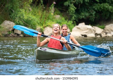 Two smiling young women kayaking down a river - Shutterstock ID 153984395