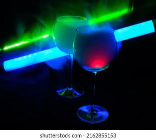 Two Smoky Cocktails With A Neon Tube And Green Laser, On A Dark Background. One Of The Glasses Slowly Igniting Alcohol Inside. Dangerous Liquor Mixture - Close Up Photo. Background Picture.