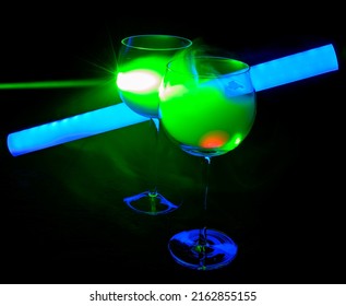 Two Smoky Cocktails With A Neon Tube And Green Laser, On A Dark Background. One Of The Glasses Slowly Igniting Alcohol Inside. Dangerous Liquor Mixture - Close Up Photo. Background Picture.