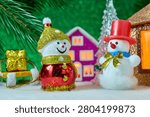 Two snowmen and a present on a sled near a Christmas lantern with a pink house in the background