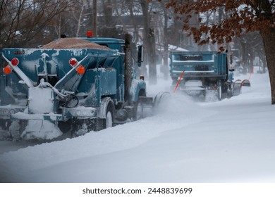 Two snowplows working bakc to back clearing snow and dropping sand at the end of a blizzard in Babylon New York Long Island