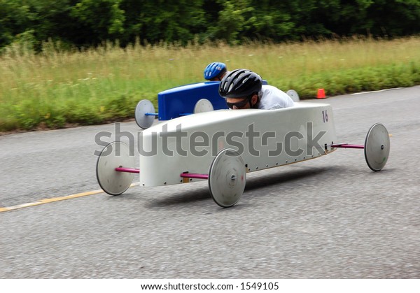 Two soap box derby\
cars speed down a track. Panning and medium shutter convey high\
speed and wheel rotation