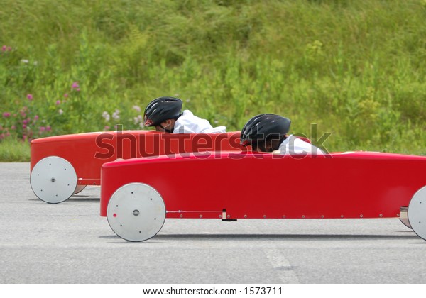 Two soap box derby cars neck and neck as they cross\
the finish line.