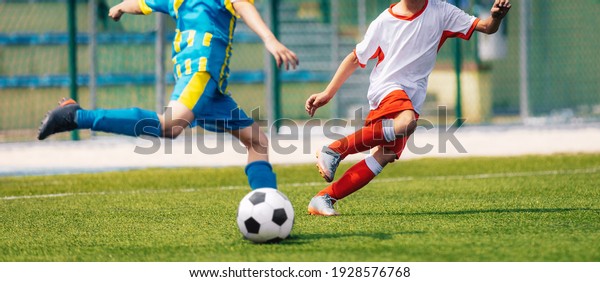 Two Soccer Boys Kicking Ball in Opposite Teams.\
Football Duel; Kicking Ball Moment. Young Football Players Running\
in Duel and Playing Soccer Tournament Match. Sports Competition for\
Youth Athletes
